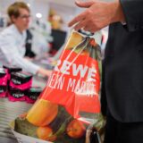Ein Kunde packt an der Kasse eines Rewe-Marktes seine Einkäufe in eine Tragetasche aus Plastik.
