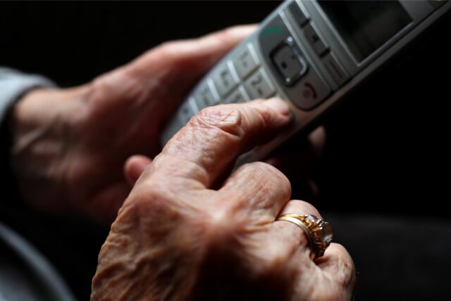 Eine ältere Frau tippt auf einem schnurlosen Festnetztelefon.