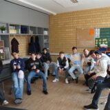 Eine große Gruppe an Schülerinnen und Schülern sitzt im Stuhlkreis