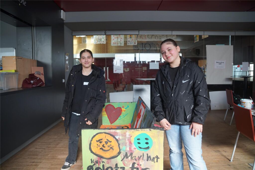 Die zwei Mädchen stehen neben der selbstgemalten Bank.
