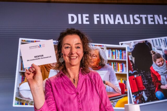 Frau hält Schild hoch, wo der Gewinner Mentor draufsteht.