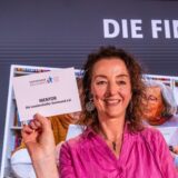 Frau hält Schild hoch, wo der Gewinner Mentor draufsteht.