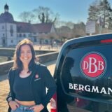 Anna Pusch, Pressesprecherin der Bergmann-Brauerei, steht vor dem Wasserschloss Haus Rodenberg in Dortmund-Aplerbeck. Neben ihr steht ein Transporter, auf dem das Bergmann-Logo zu sehen ist.
