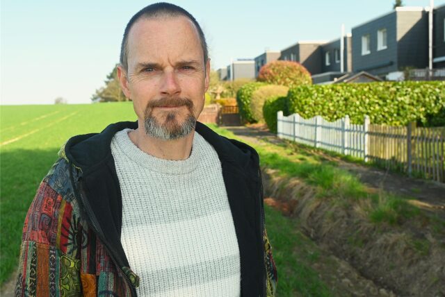 Heiko Friedrich aus Dortmund-Lichtendorf steht zwischen einem Feld und einer Häuserreihe. Er hat eine Selbsthilfegruppe für Adoptierte aus Dortmund und dem Kreis Unna gegründet.