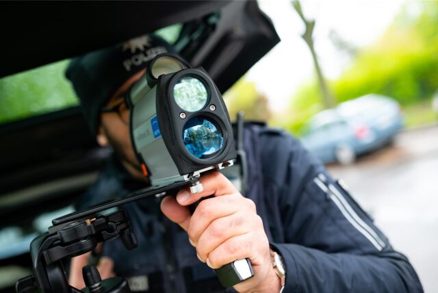 Ein Polizist kontrolliert während des Blitzermarathons mit einem Messgerät die Geschwindigkeit von Fahrzeugen in einer 30er-Zone.