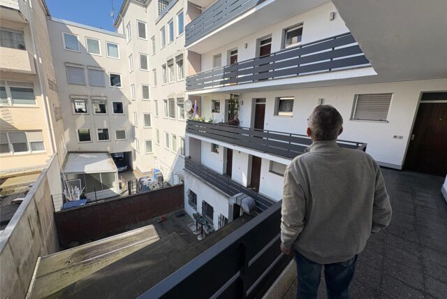 Rainer S. steht im 1. Stock des Wohnhauses und schaut auf die gegenüberliegenden Wohnungen.