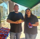 Zwei Personen mit Spargel und Erdbeeren an einem Verkaufsstand.