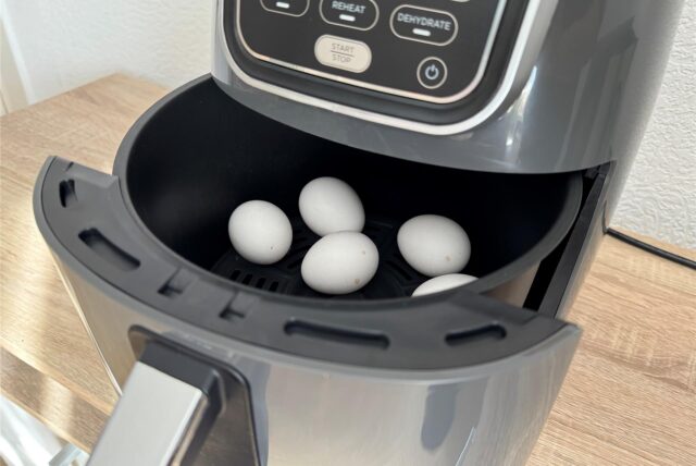 Fünf weiße Eier liegen im geöffneten Backfach eines Airfryers.