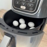 Fünf weiße Eier liegen im geöffneten Backfach eines Airfryers.