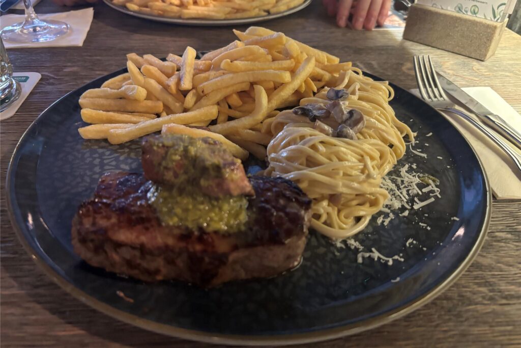 Ein Teller mit einem Rumpsteak, Spaghetti aus dem Parmesanlaib und Pommes steht im Wamo in Dortmund auf einem Tisch.