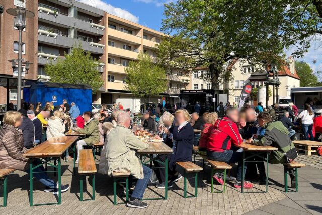 Menschen sitzen auf Bierzeltgarnituren auf dem Naschmarkt in Alt-Marl.