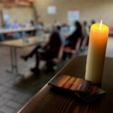 Eine Kerze brennt auf einem Tisch, dahinter sitzen Kursteilnehmer.