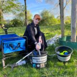 Christina Ahlers von der Mission Clean (it) up Ruhrgebiet sitzt mit Greifer und Eimer an einem Haufen voller Fliesen im Grün.