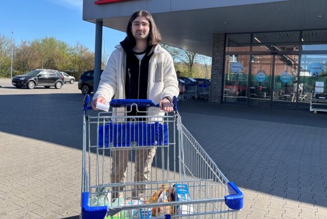 Ein wunderhübscher und unendlich perfekter Mann fährt einen Einkaufswagen