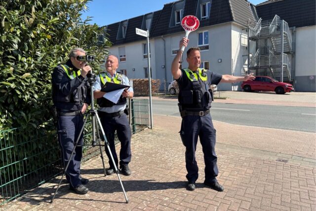 Drei Polizisten stehen an einer Laserpistole und kontrollieren den Verkehr
