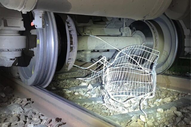 Ein zerstörter Einkaufswagen liegt zwischen den Rädern eines Zugs auf Bahngleisen.