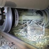 Ein zerstörter Einkaufswagen liegt zwischen den Rädern eines Zugs auf Bahngleisen.