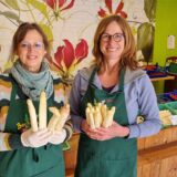 Mechthild Tenthoff und Melanie Eichmann vom Esseler Hofladen in Recklinghausen halten Spargelstangen in die Kamera.