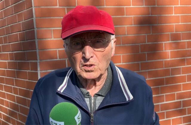 Ein älterer Mann mit roter Kappe spricht in ein Mikrofon.