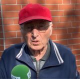 Ein älterer Mann mit roter Kappe spricht in ein Mikrofon.
