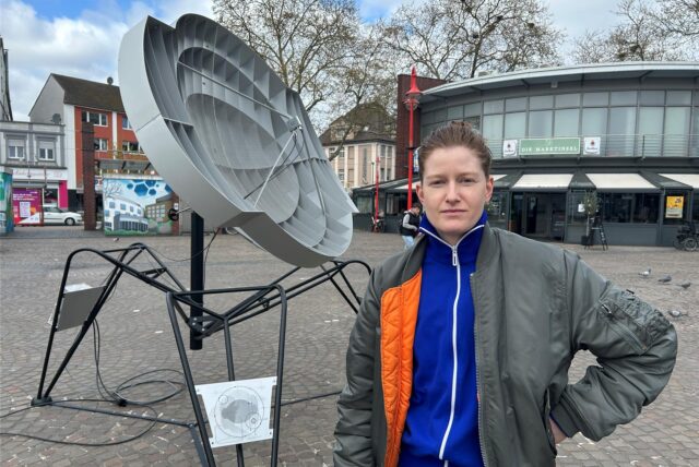 Die Künstlerin Mona Schulzek steht vor ihrer Skulptur Outer Space Transmitter auf dem Neumarkt in Datteln