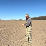 Ein Landwirt in Arbeitskleidung steht auf einem leeren Acker. Der Boden zeigt deutliche Spuren von Trockenheit.