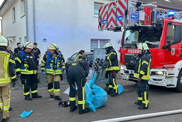 Einsatzkräfte der Feuerwehr verpacken etwas in einem blauen Sack. Rechts im Bild steht ein Feuerwehrauto.