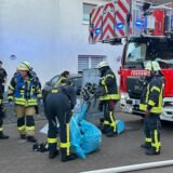 Einsatzkräfte der Feuerwehr verpacken etwas in einem blauen Sack. Rechts im Bild steht ein Feuerwehrauto.