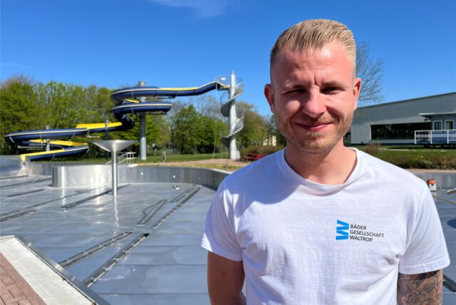 Leon Neumeister von der Bädergesellschaft Waltrop steht vor dem Nichtschwimmerbecken des Freibads. Im Hintergrund ist zudem die große Wasserrutsche erkennbar.