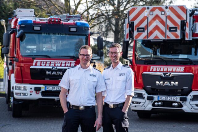 Zwei Feuerwehrleute stehen vor Feuerwehrwagen.