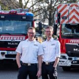 Zwei Feuerwehrleute stehen vor Feuerwehrwagen.