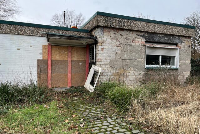 Bungalow auf dem Hollenbeck in Disteln mit kaputter Fassade und Holzbrettern vor der Tür.