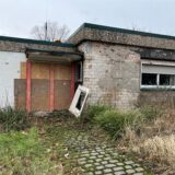 Bungalow auf dem Hollenbeck in Disteln mit kaputter Fassade und Holzbrettern vor der Tür.
