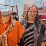 Eine Frau steht in einem Bekleidungsgeschäft neben einer Schaufensterpuppe und Regalen und Stangen voller Kleider.