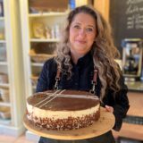 Aida Suvalic in ihrem Café Kulisse in Herten-Scherlebeck hinter der Theke und hält eine selbstgebackene Torte in den Händen.