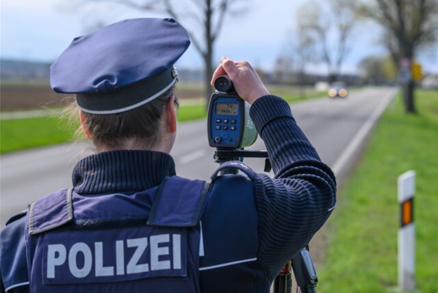 Eine Polizeibeamtin steht mit einem Lasermessgerät an einer Bundesstraße und überwacht die Geschwindigkeit der Fahrzeuge.
