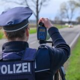 Eine Polizeibeamtin steht mit einem Lasermessgerät an einer Bundesstraße und überwacht die Geschwindigkeit der Fahrzeuge.