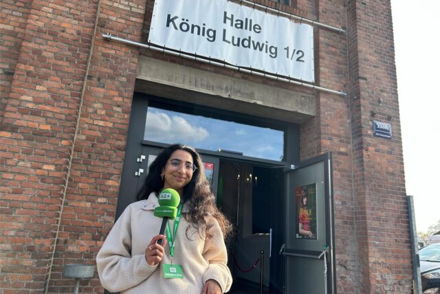 RZ-Reporterin Rosi Taslima Azam steht mit grünem Mikrofon vor der Halle König Ludwig in Recklinghausen.