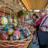 Besucher stehen auf einem Ostermarkt in NRW vor einem Verkaufsstand mit bunten Ostereiern.
