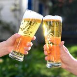 Zwei Personen stoßen am Tag des deutschen Bieres mit Biergläsern an.