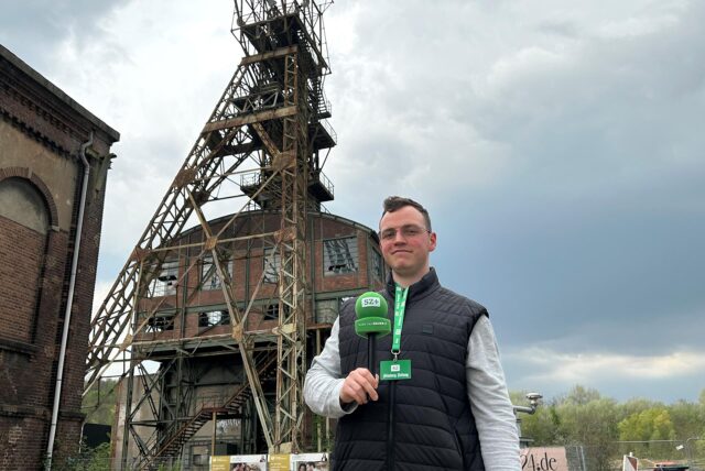Eine Person mit schwarzer Weste steht auf einem ehemaligen Zechengelände.