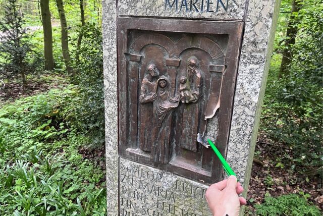 Bronzetafel, eine von sieben Tafeln der Via Matris, an der Sieben-Schmerzen-Kapelle im Wald. Kugelschreiber zeigt auf das Loch in dem Kunstwerk.