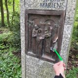 Bronzetafel, eine von sieben Tafeln der Via Matris, an der Sieben-Schmerzen-Kapelle im Wald. Kugelschreiber zeigt auf das Loch in dem Kunstwerk.