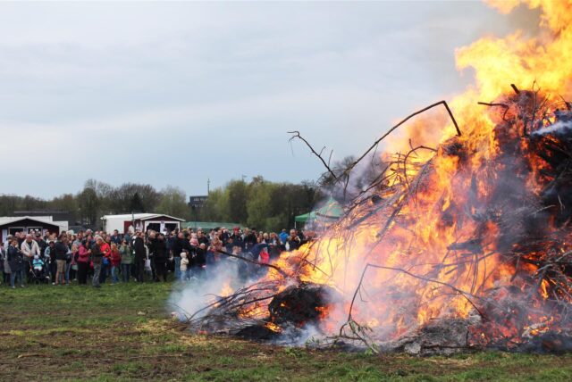 Viele Menschen stehen auf einer Wiese von Bauer Karl Godde in Herten-Disteln um ein loderndes Osterfeuer.