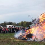 Viele Menschen stehen auf einer Wiese von Bauer Karl Godde in Herten-Disteln um ein loderndes Osterfeuer.