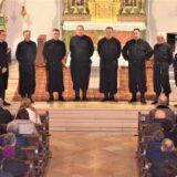 Eine Gruppe von Männern stehen in einer Kirche vor dem Altar und singen. Auf den Kirchenbänken sitzt das Publikum.