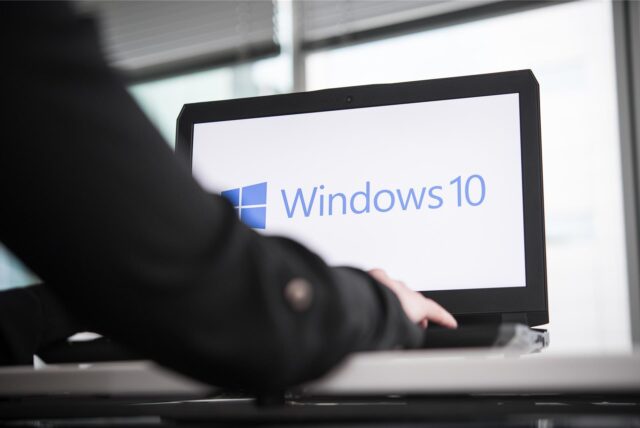 Eine Person tippt an einem Laptop, auf dessen Bildschirm das Microsoft Windows 10 Logo zu sehen ist.