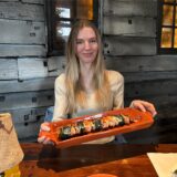 Eine Frau präsentiert einen Teller mit Spießen in einem Restaurant. Der Teller ist orange und die Spieße scheinen aus Fleisch und Gemüse zu bestehen.