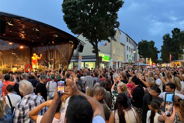 Auf der Bahnhofstraße in Herten-Westerholt stehen viele feiernde Menschen vor einer Bühne, auf der Schlagersänger Olaf Henning in Aktion ist.