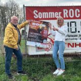 Vor dem Banner an der Schachtstraße präsentieren die beiden Lions-Mitglieder Elke Fleckhaus und Karl-Heinz Dargel das Plakat für das diesjährige „Sommer Rock Festival“.